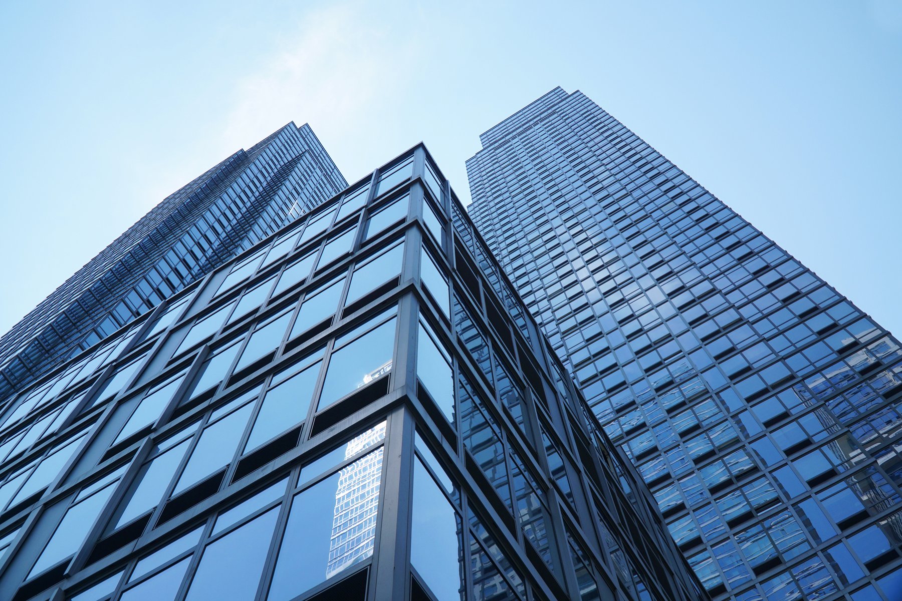 Alt text: "Upward view of tall modern skyscrapers with reflective glass facades, emphasizing vertical lines and urban sophistication